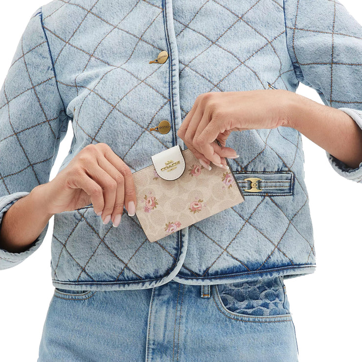 Model Holding Coach Medium Corner Zip Wallet In Signature Canvas With Floral Print - Sand Multi CAR13