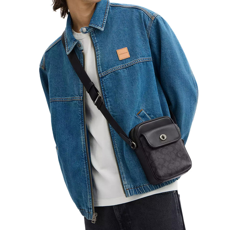 Male Model carrying Coach Turnlock Crossbody Bag In Signature Canvas - Charcoal/ Black CAJ30, across his body
